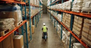 Worker in warehouse aisle with boxes on shelves.