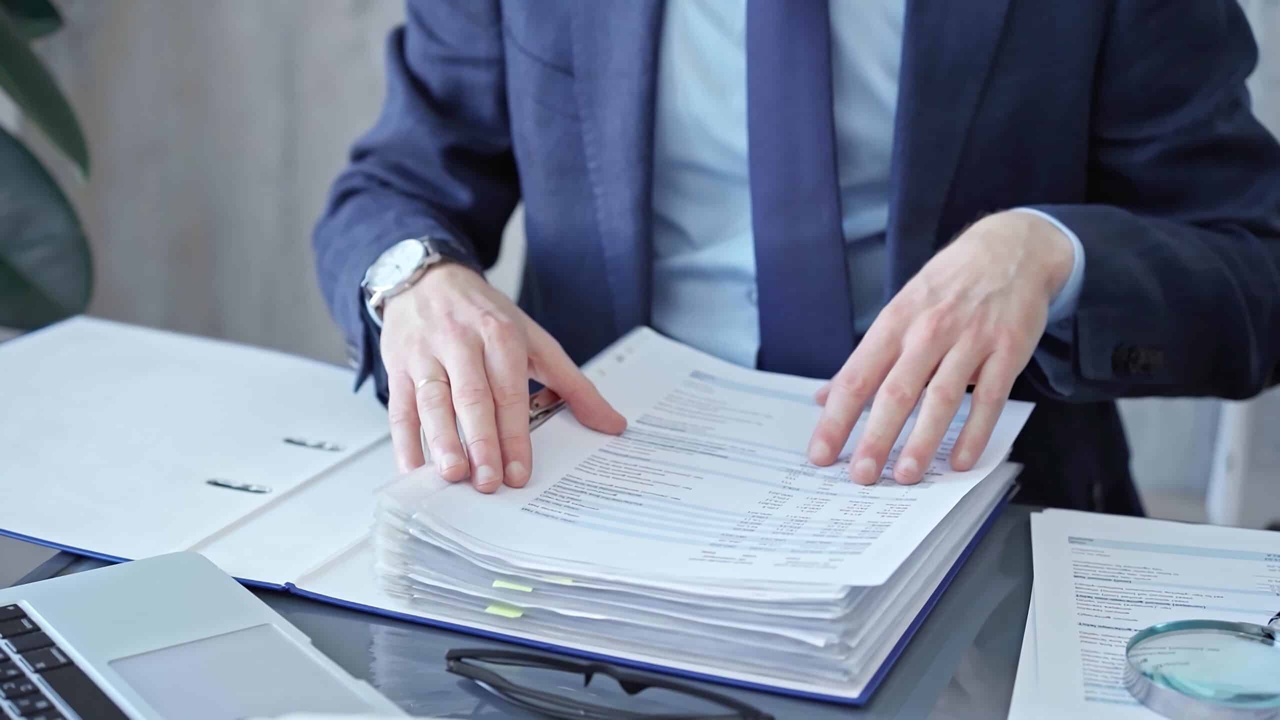 Professional reviewing documents on a glass desk.