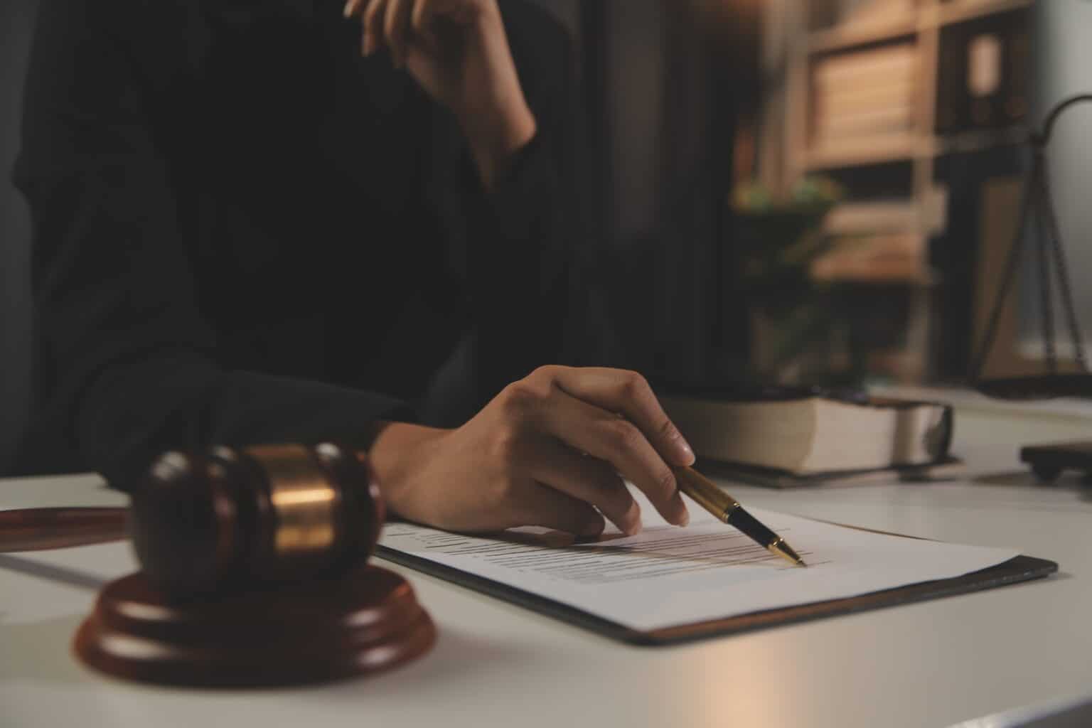 Hand writing on legal document with gavel nearby.