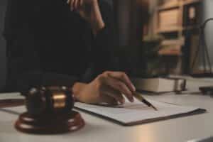Hand writing on legal document with gavel nearby.