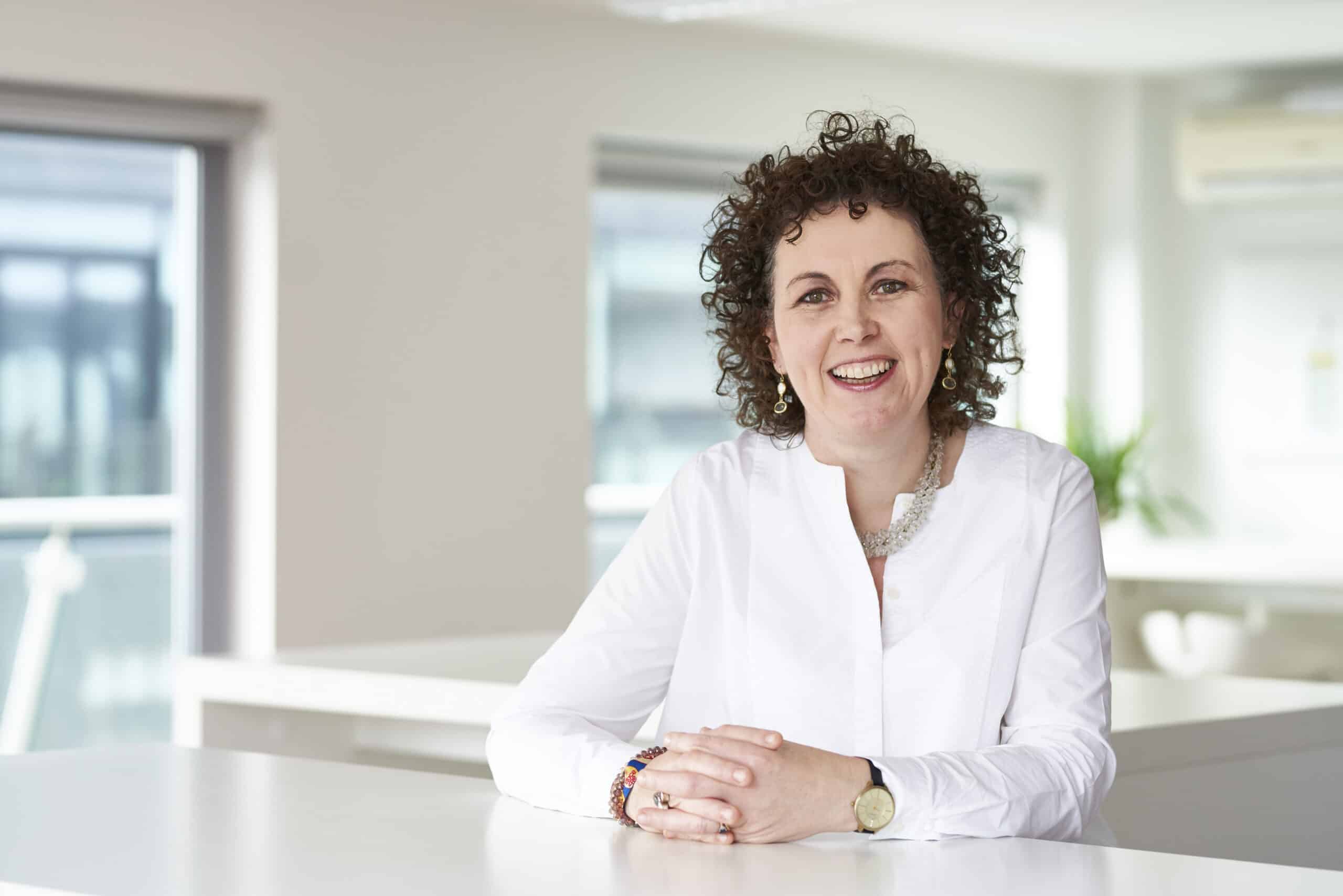Smiling woman sitting at a bright office desk.