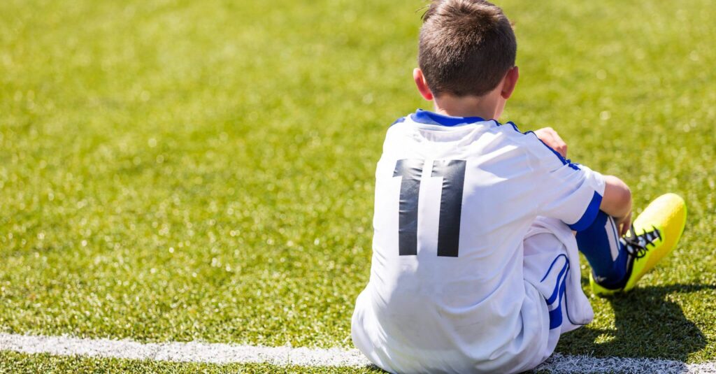 Soccer player in white jersey sitting on field.