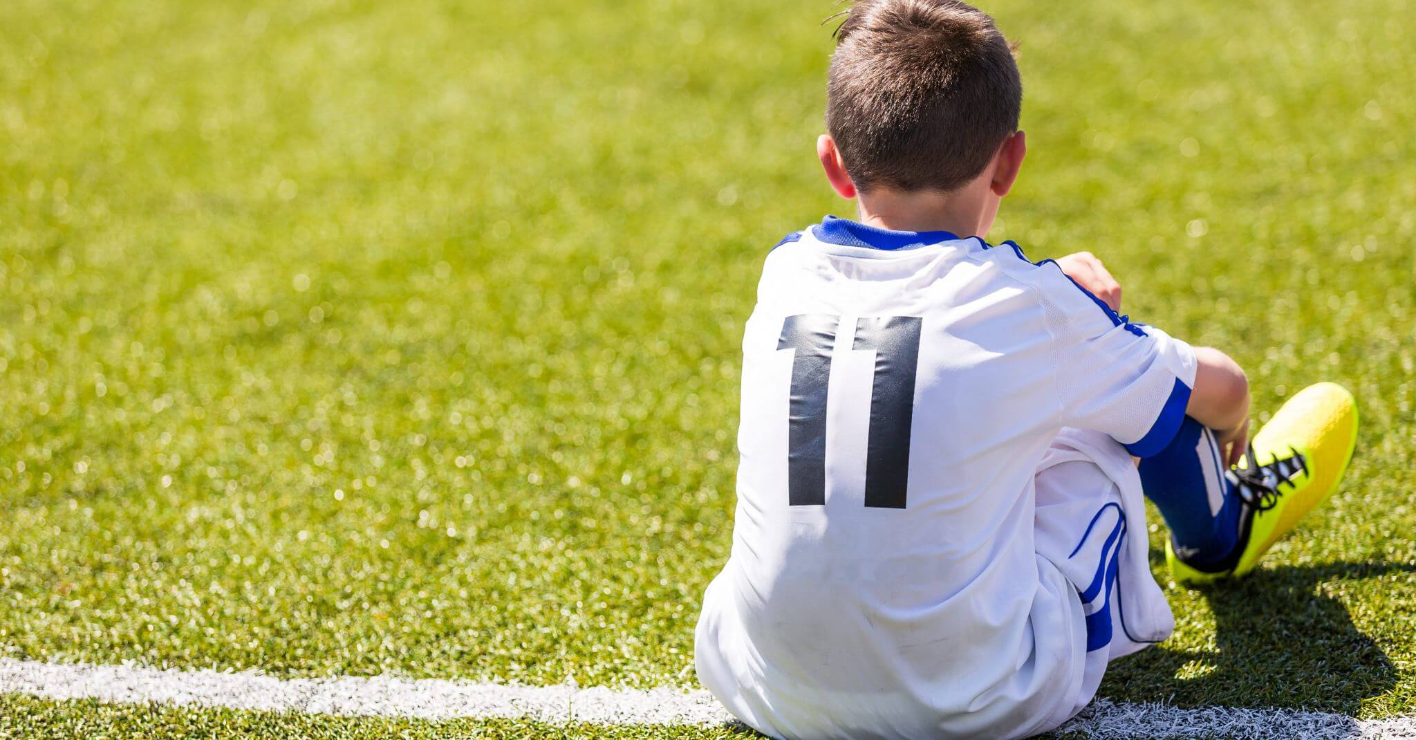 Soccer player in white jersey sitting on field.