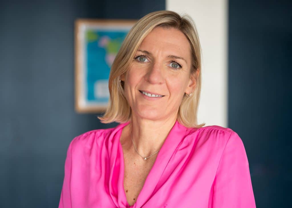 Smiling woman in pink blouse, blue background.