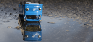 blue toy VW van upside down in a puddle with a reflection of the van the right way round