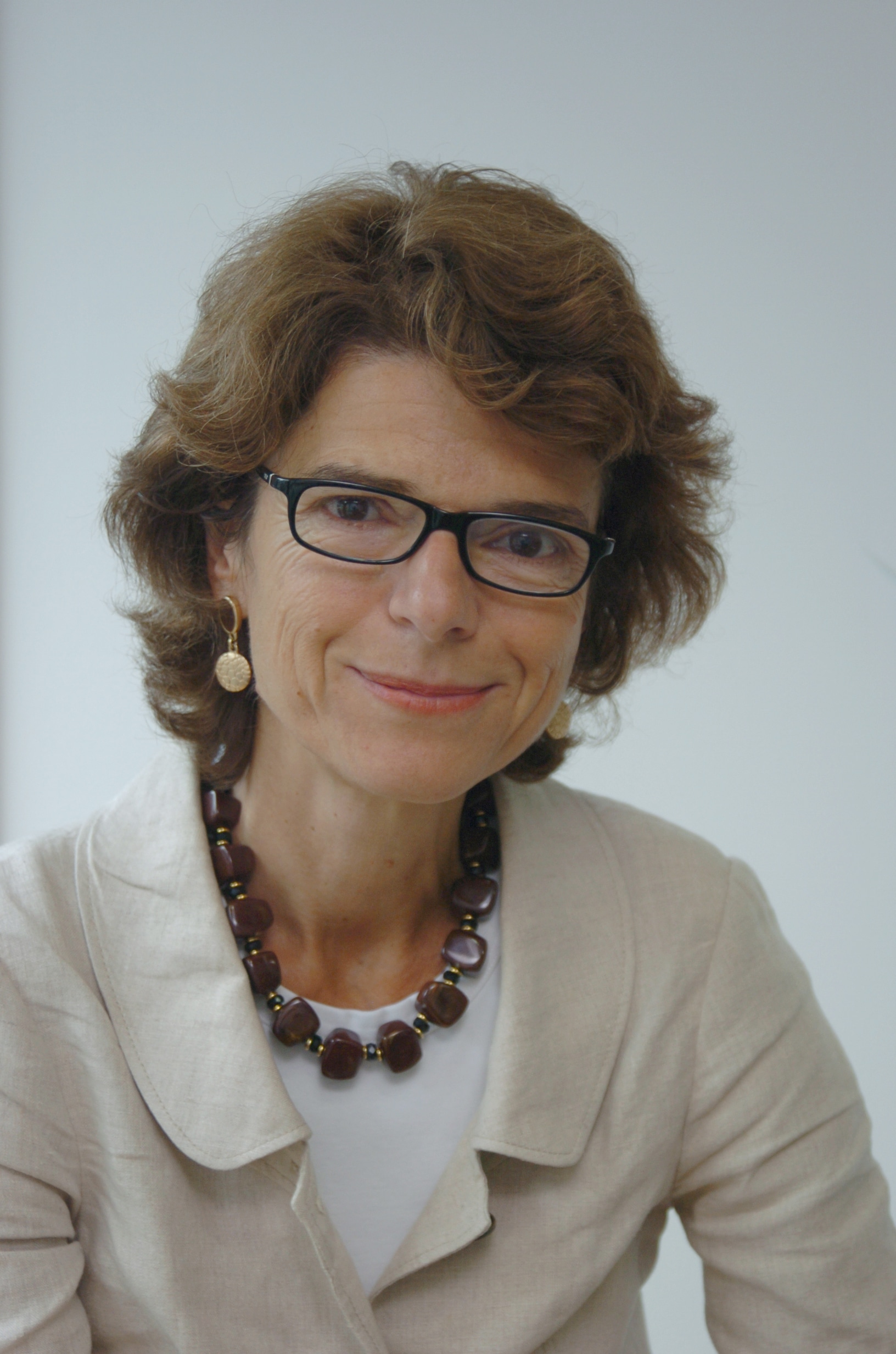 Woman with glasses and brown necklace, smiling.