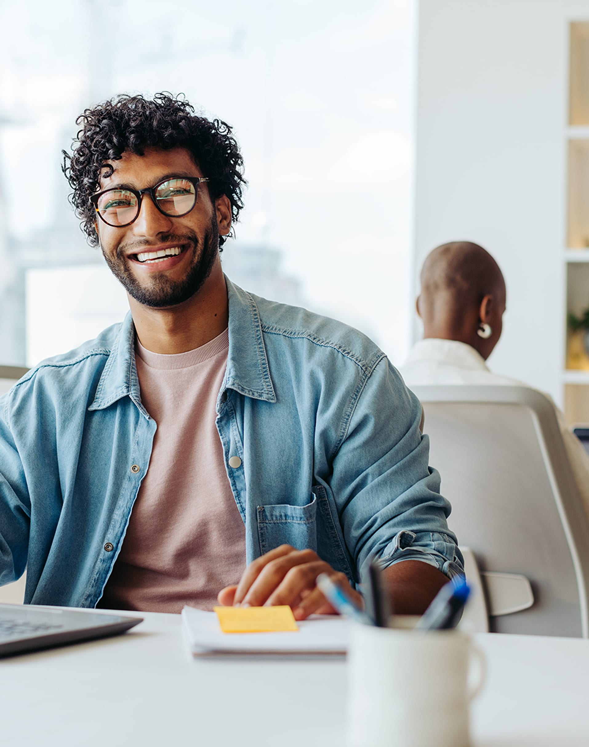 Smiling man in office with laptop and notes.