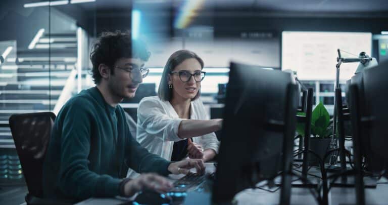 Two colleagues collaborate at computer workstations.