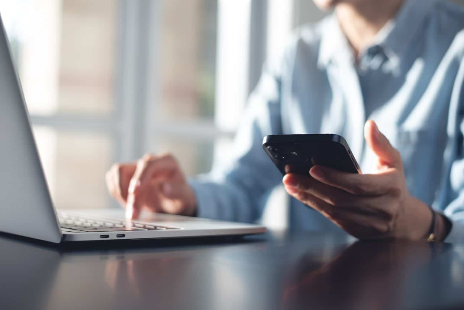 Person using laptop and smartphone at a desk.