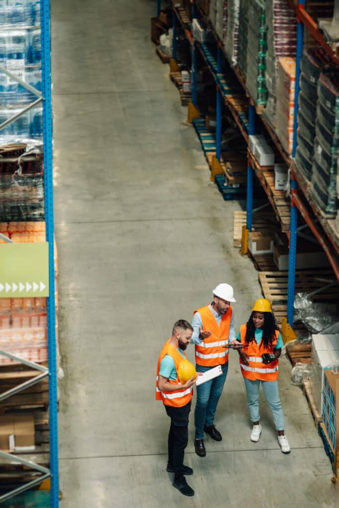 Three workers discussing in a warehouse aisle