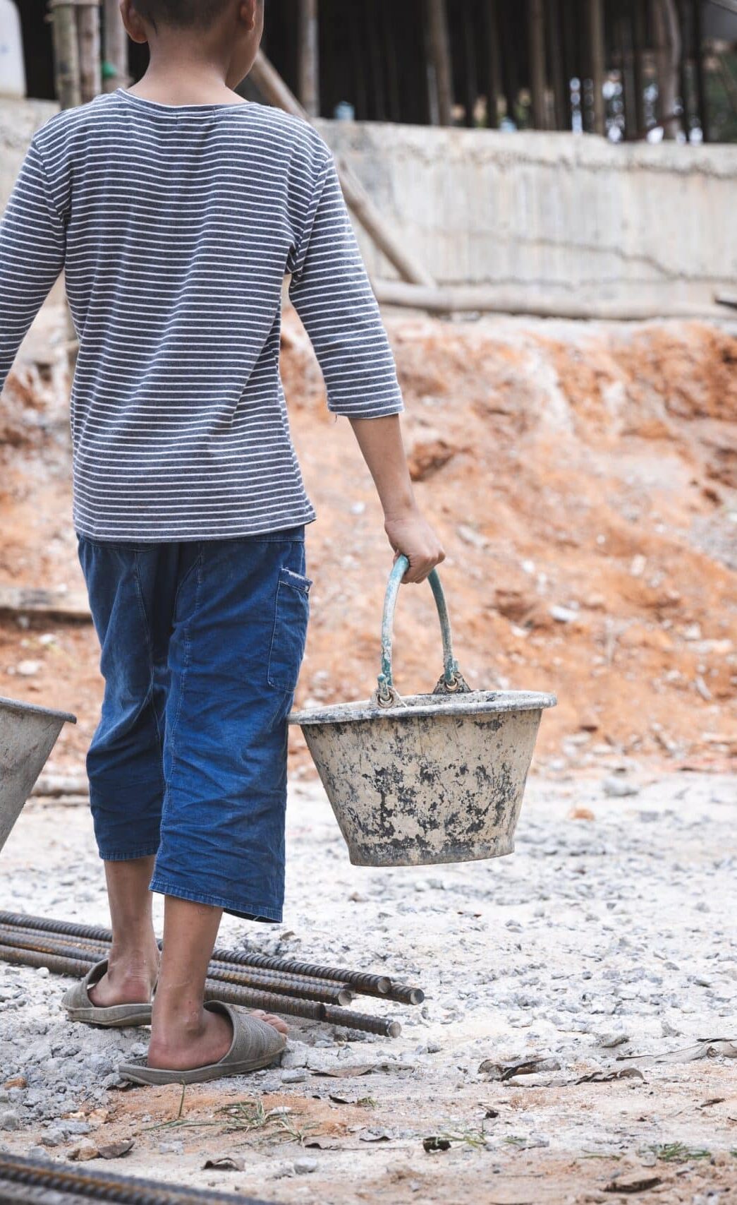 Child carrying buckets at a construction site.