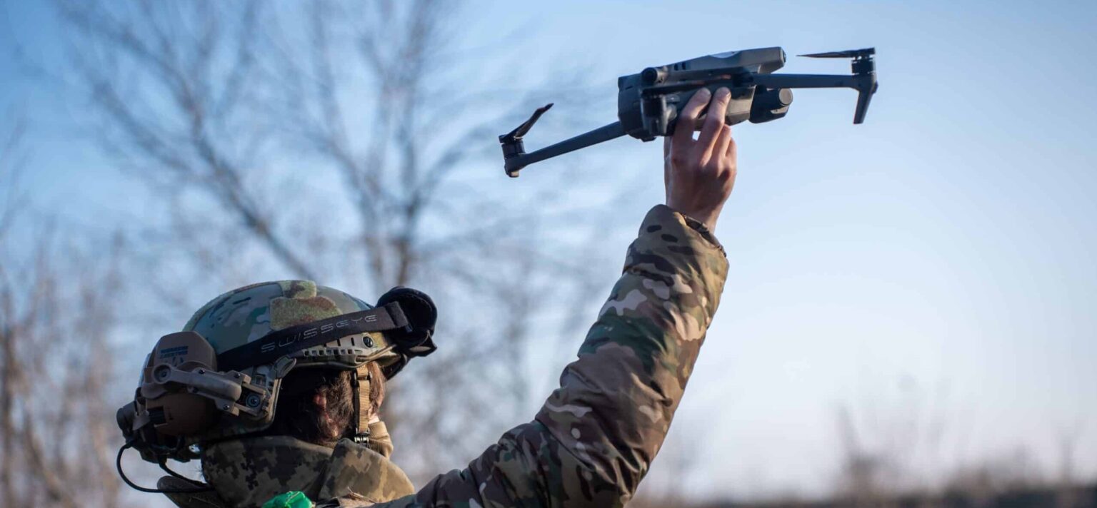 Soldier launching a drone in open terrain.