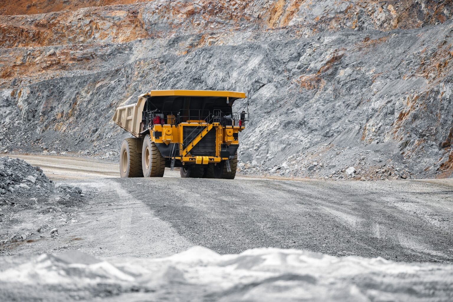 Large yellow dump truck on gravel road in quarry