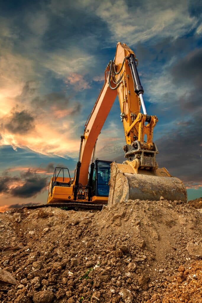Yellow excavator on dirt mound at sunset
