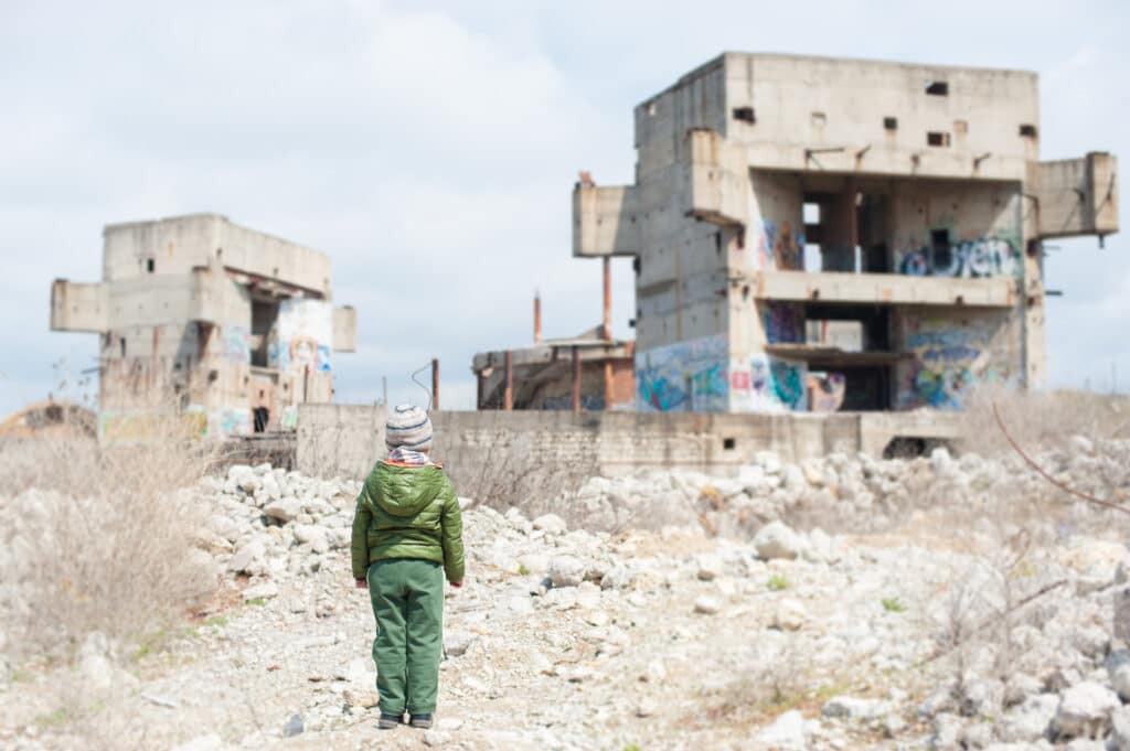 Child facing abandoned concrete buildings in rocky landscape