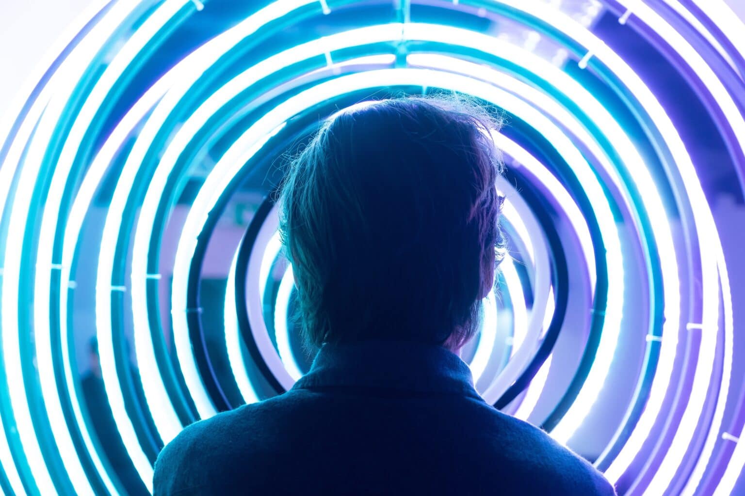 Person silhouetted against glowing neon light rings