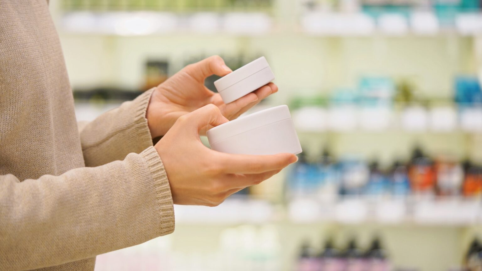 Person comparing two skincare cream jars in store